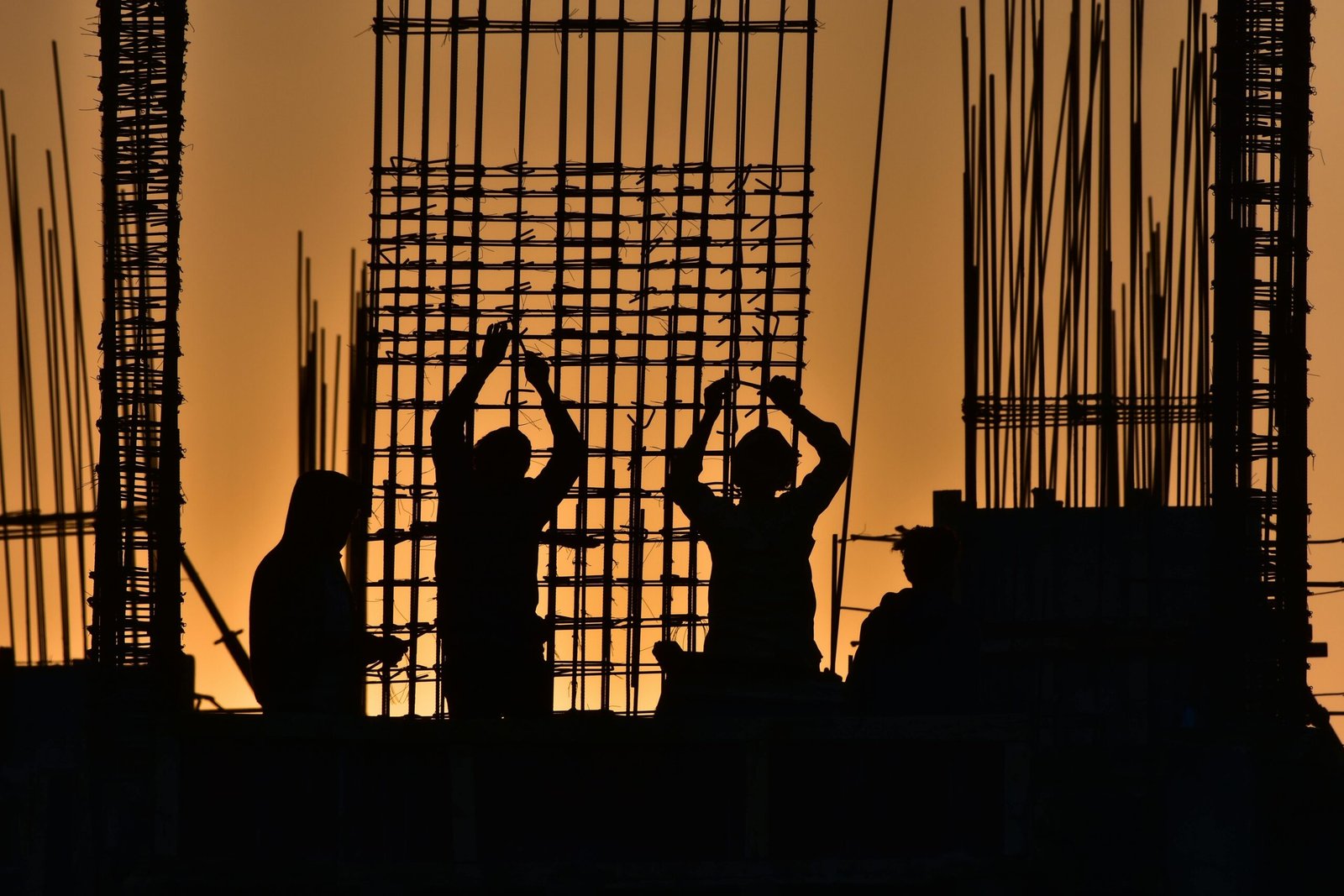 Silhouetted construction workers at a site during sunset, creating a dramatic scene.