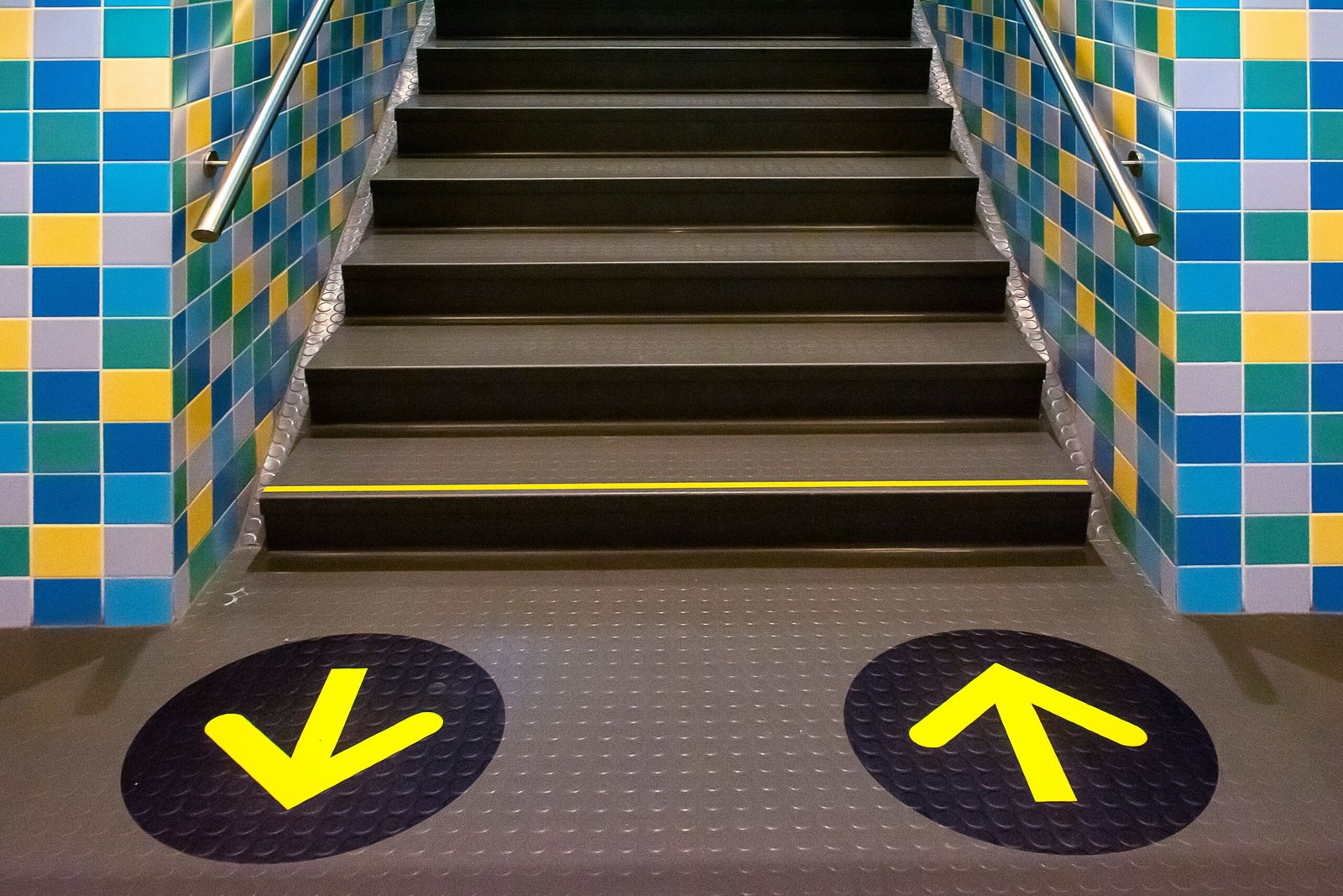 Vibrant subway stairs with yellow arrows indicate direction amidst blue and yellow tiles.